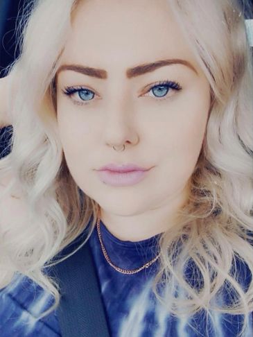 Woman with blonde hair and blue eyes wearing a seatbelt.