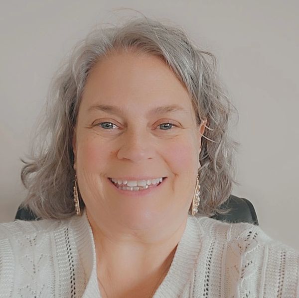 Smiling woman with gray hair and earrings wearing a white sweater.