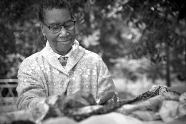 Elderly woman sewing outdoors.