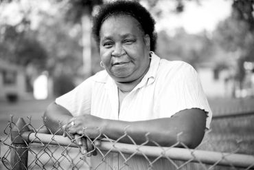 Woman leaning on a chain-link fence, smiling.