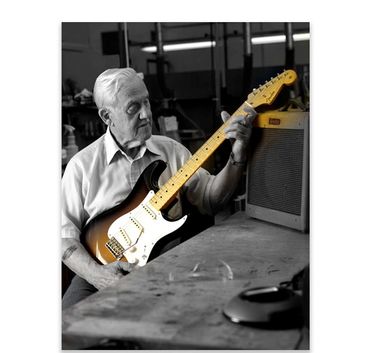 An elderly man playing an electric guitar in a workshop.