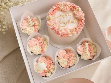 Elegant pink and white birthday cake set with cupcakes.