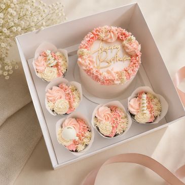 Elegant pink and white birthday cake with matching cupcakes in a box.