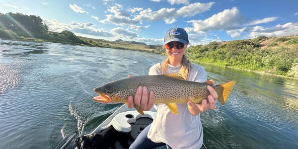Woman proudly holding a large trout on a boat in a river.