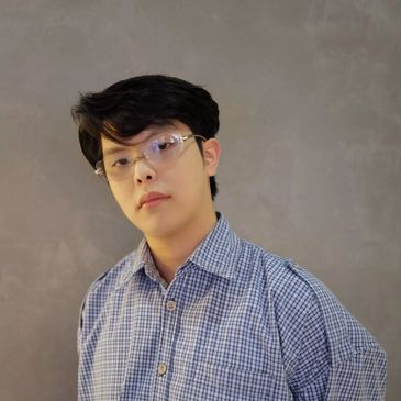 Young man wearing glasses and a checkered shirt against a gray background.