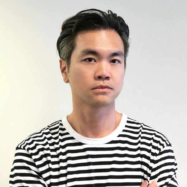 Serious man in black and white striped shirt against plain background.