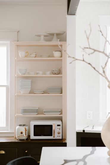 Minimalist kitchen shelves with white dishes, microwave, and toaster.