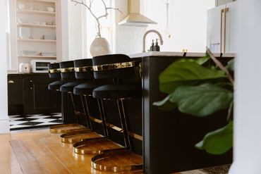Modern kitchen with black and gold bar stools along a black island.