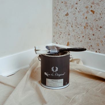 Paintbrush resting on an open paint can on a drop cloth in a corner.