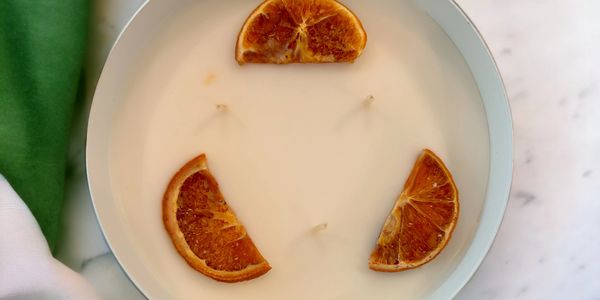 A white candle with three wicks and dried orange slices inside a light blue container.