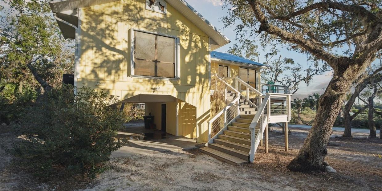 Yellow stilt house with exterior stairs and surrounding trees.