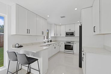 Modern white kitchen with marble countertops and black accents.
