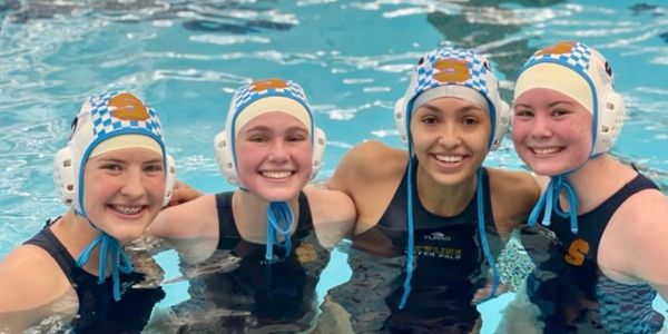 Four happy female water polo players posing in the pool.