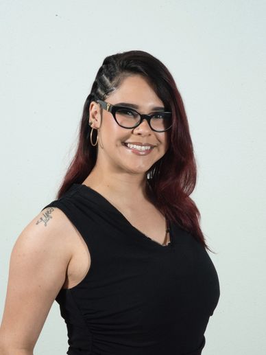 Smiling woman with glasses and braided hair wearing a black sleeveless top.