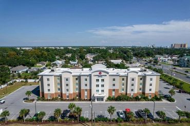 Exterior view of a Comfort Suites hotel building with parking lot and surrounding neighborhood.