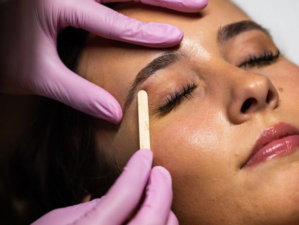 Woman getting eyebrow treatment with wooden stick.