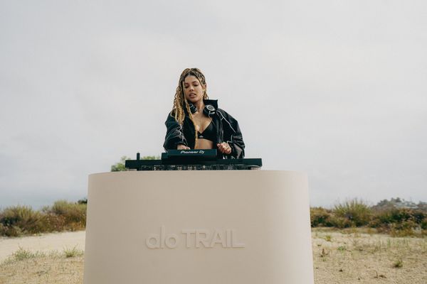 A female DJ performs outdoors behind a booth labeled 'alo TRAIL'.