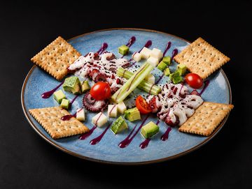 Plato de ensalada con galletas saladas, queso y vegetales.