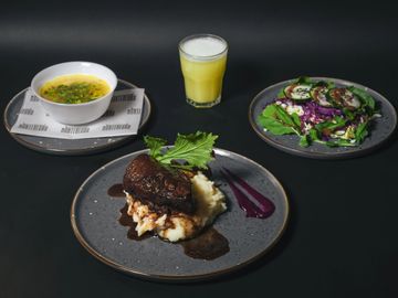 A gourmet meal with soup, salad, steak on mashed potatoes, and a glass of juice.