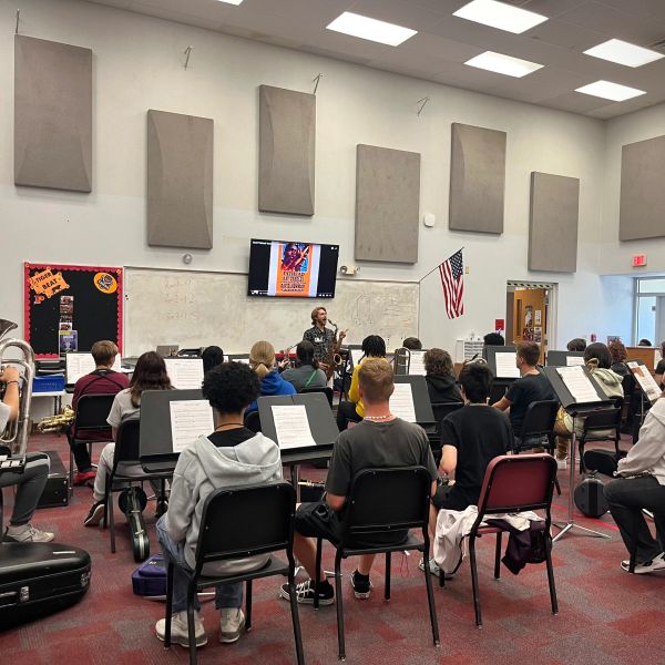 Students practicing music in a spacious classroom with a teacher conducting.