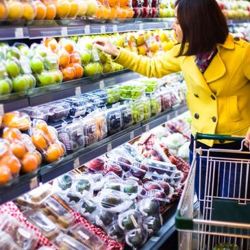 Woman in yellow coat shopping for fruits at a grocery store.