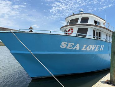 Blue boat named SEA LOVE II docked at a pier under a cloudy sky.