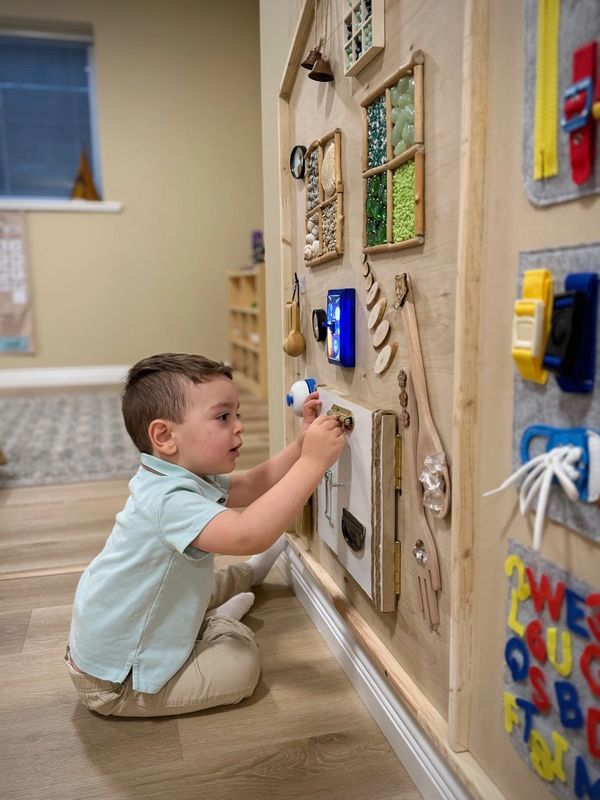 A young boy exploring a sensory activity board indoors.