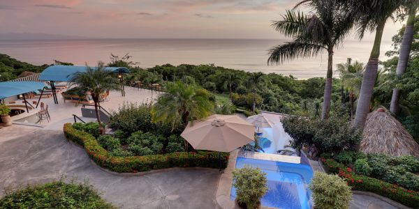 Scenic tropical resort with a pool overlooking the ocean at sunset.