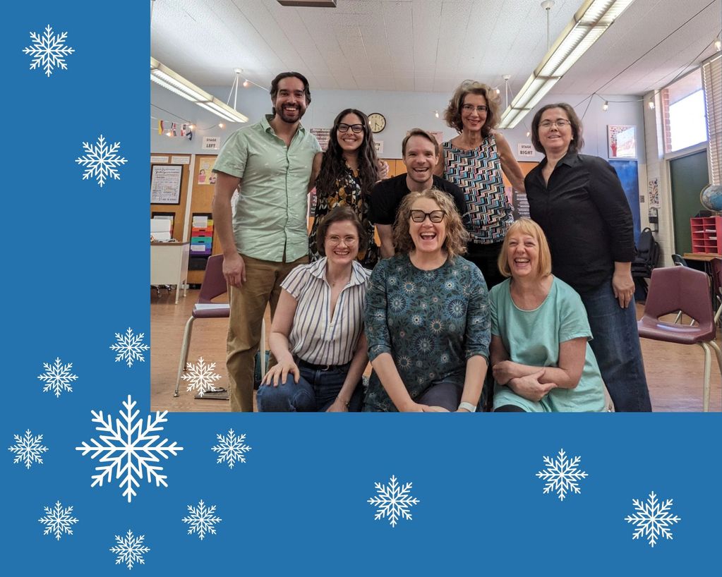 A cheerful group of eight people posing indoors with blue snowflake border.