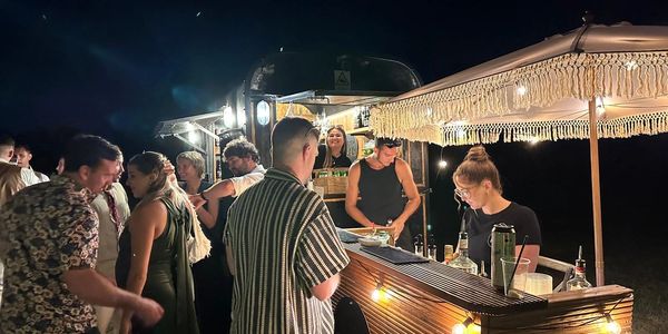 People enjoying a nighttime outdoor bar with warm lights and lively atmosphere.