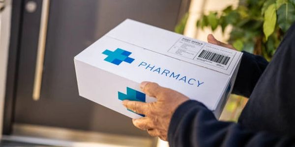 Person holding a pharmacy delivery box outside a door.