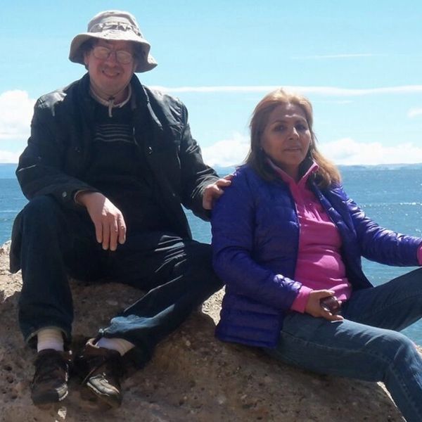 A man and woman sitting on rocks by the ocean, enjoying a sunny day.