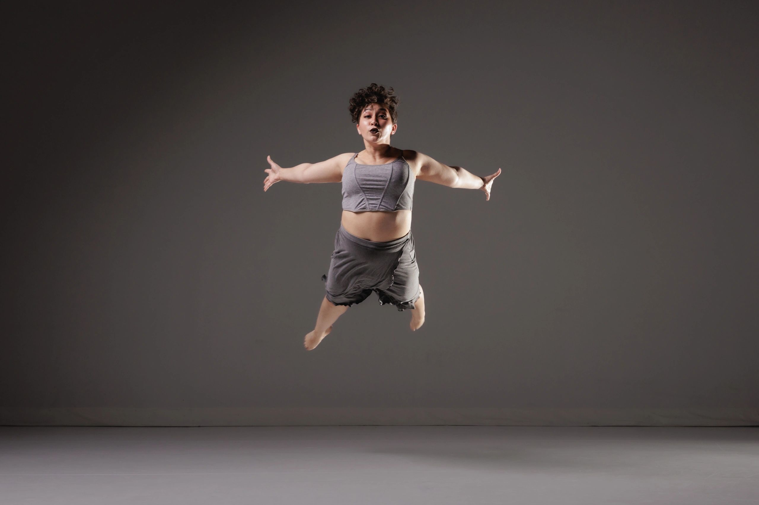 Person mid-air jumping with arms outstretched against a dark background.
