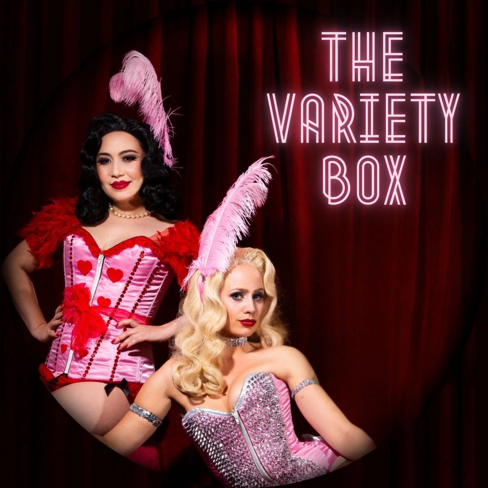 Burlesque performers Athena Beauvoir and Evelyn Carnate pose in front of a red velvet curtain.