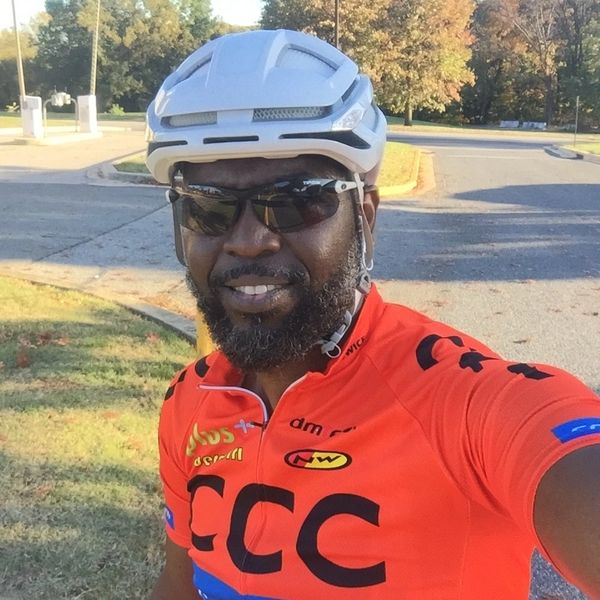 Cyclist wearing a white helmet and orange jersey outdoors.