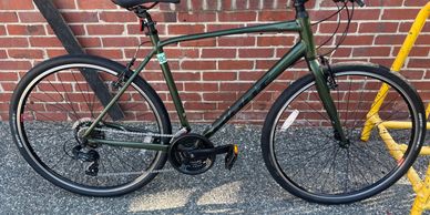 A green road bike parked against a brick wall with yellow bike rack.