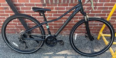 Black bicycle parked against a brick wall and yellow bike rack.