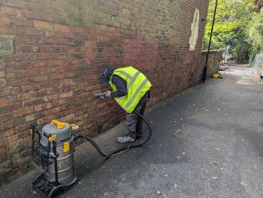 Worker cleaning brick wall with vacuum device.