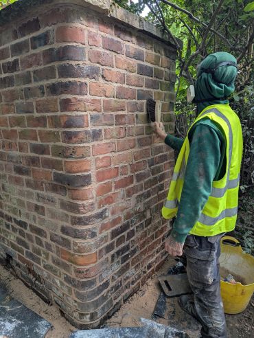 Worker cleaning brick wall wearing reflective vest and head covering.