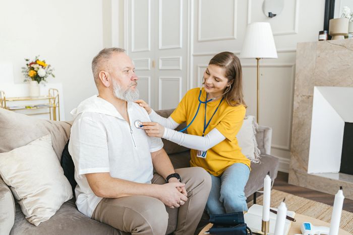 women in yellow shirt holding a stethoscope to a elderly mans chest