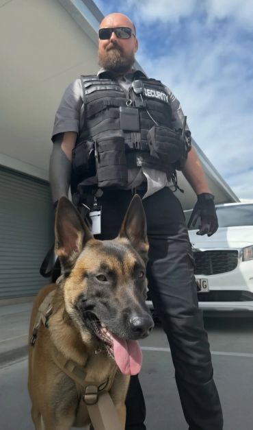 Security guard with a trained dog outside a building on a clear day.