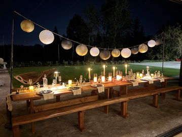 Outdoor wooden table set with candles and hanging lanterns at night.