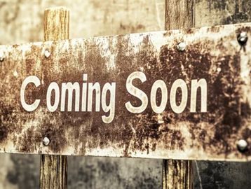 Rusty metal sign with 'Coming Soon' text on wooden posts.
