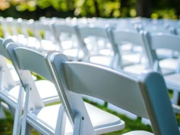 Rows of white folding chairs set up outdoors on green grass.