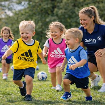Young children playing soccer with a smiling coach outdoors.