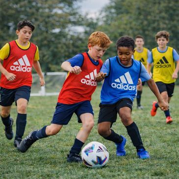 Kids playing soccer in colorful Adidas jerseys on a grassy field.