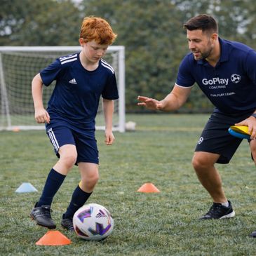 Young boy practicing soccer with coach on field.