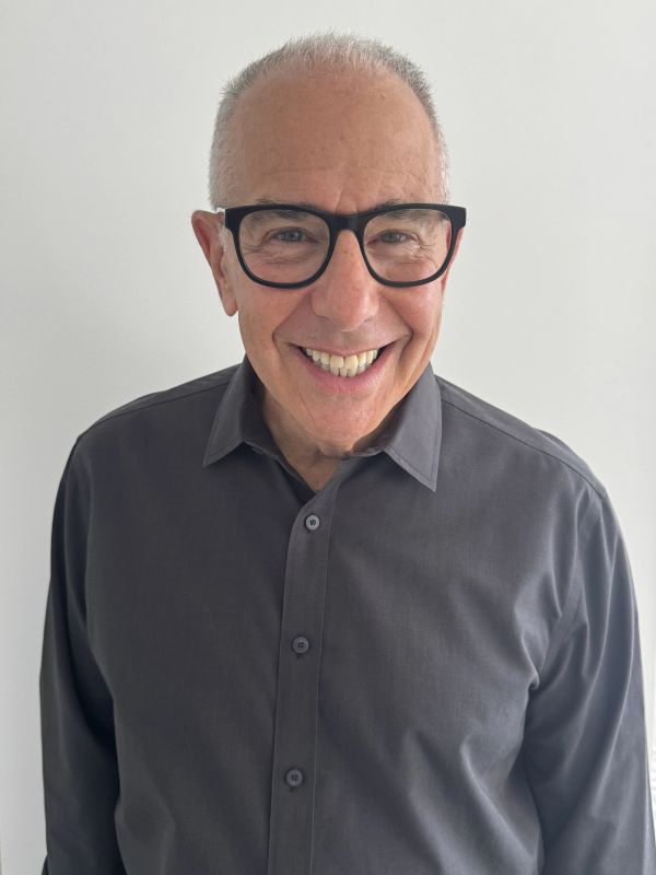 Smiling older man with glasses and gray shirt.