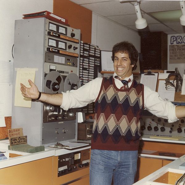 Man smiling with arms open in a vintage radio station studio.
