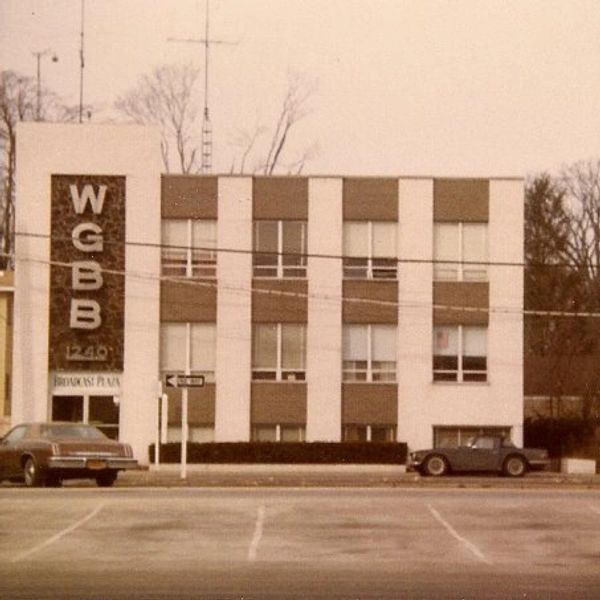 Vintage photo of WGBB radio station building with classic cars parked outside.